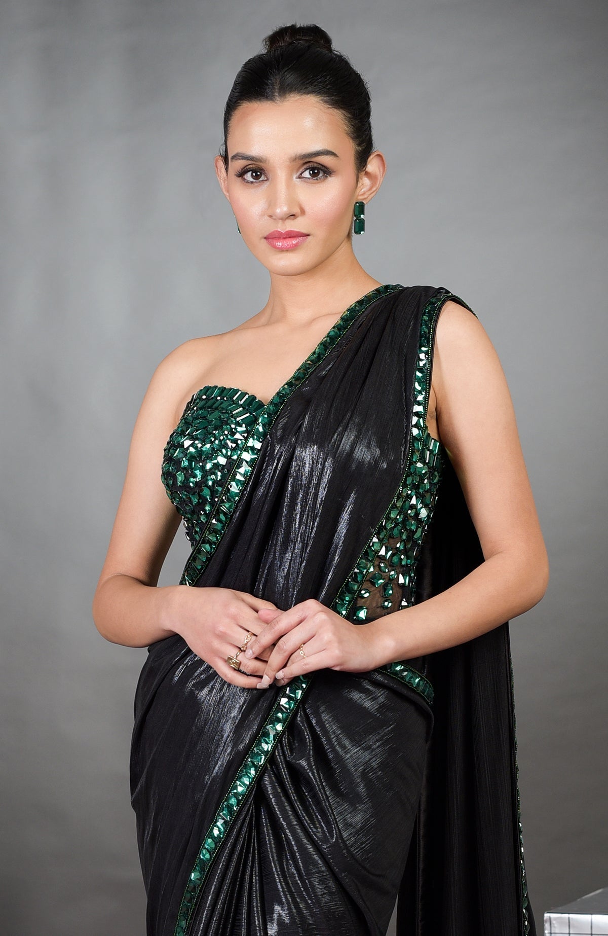 A woman models a black saree with an emerald green embroidered corset and matching earrings.