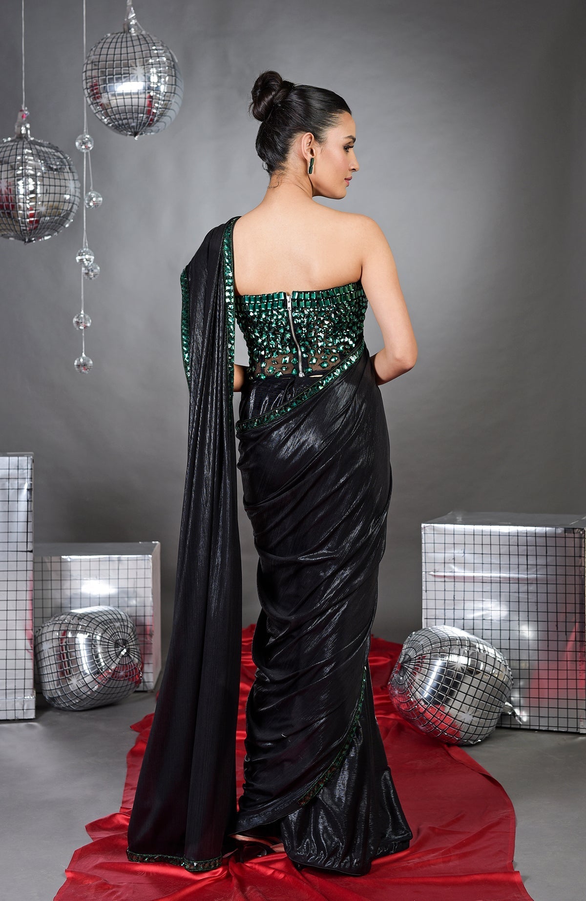 A woman models a black saree with an emerald green embroidered corset from the back.