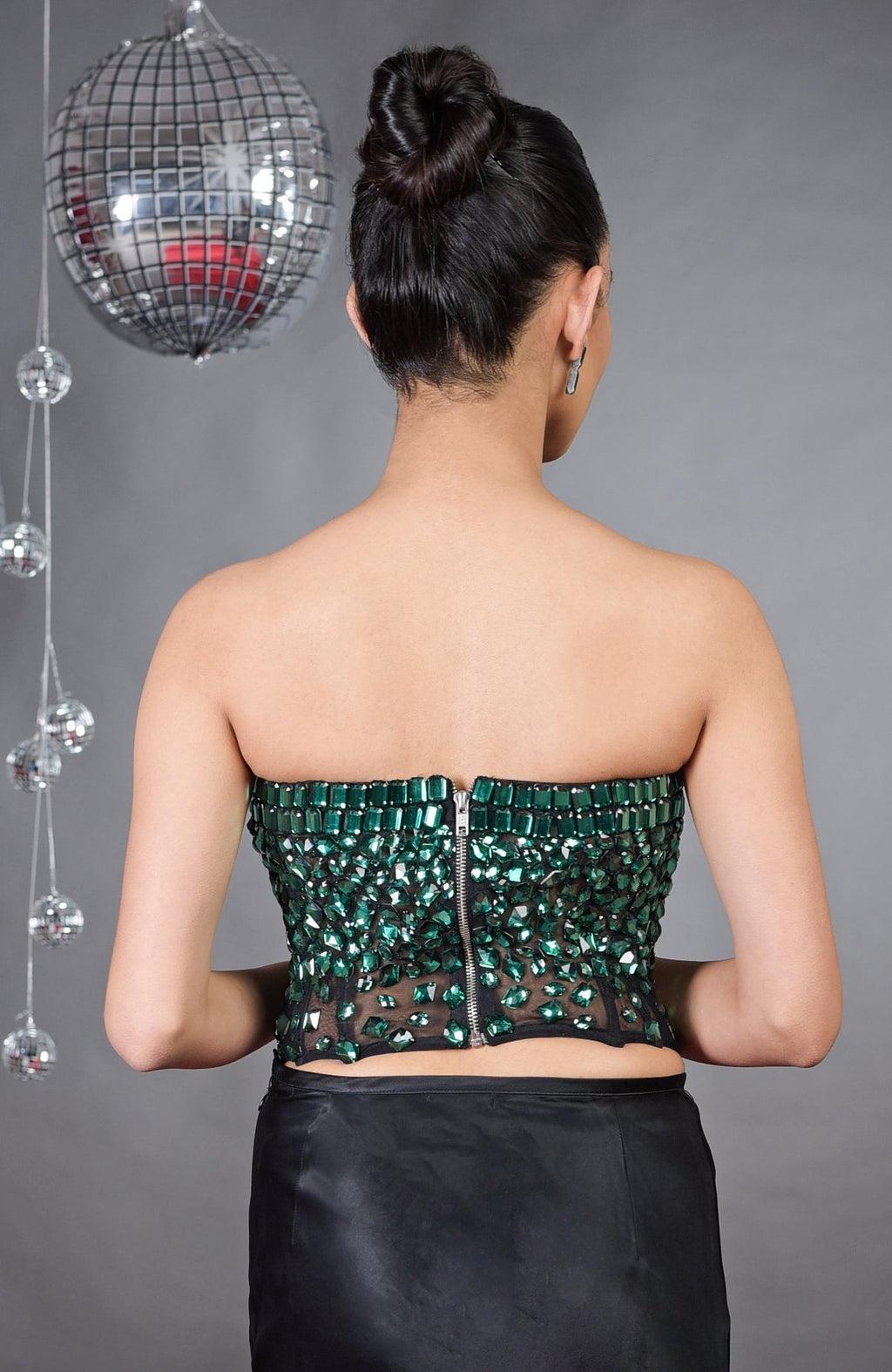 A woman from behind wears an emerald green hand-embroidered corset and black skirt.