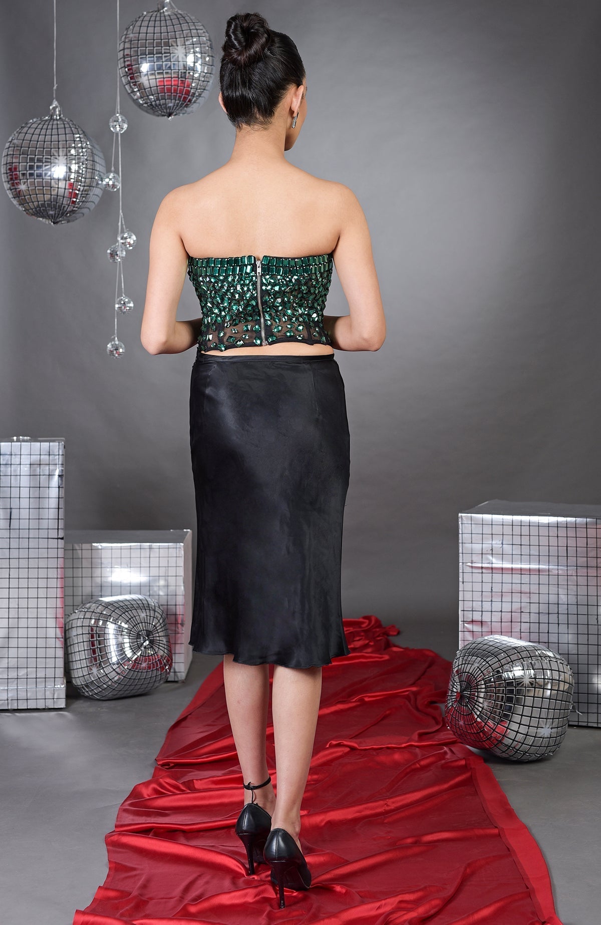 A woman from behind wears an emerald green hand-embroidered corset and a black skirt.