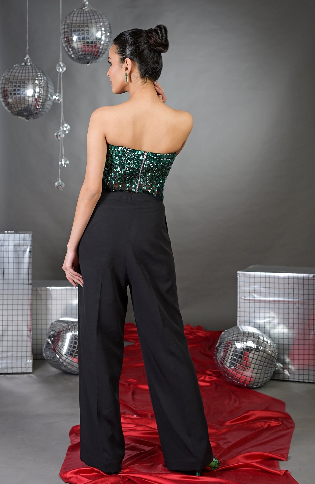 A woman from behind wears a green sequined corset and black wide-leg pants.