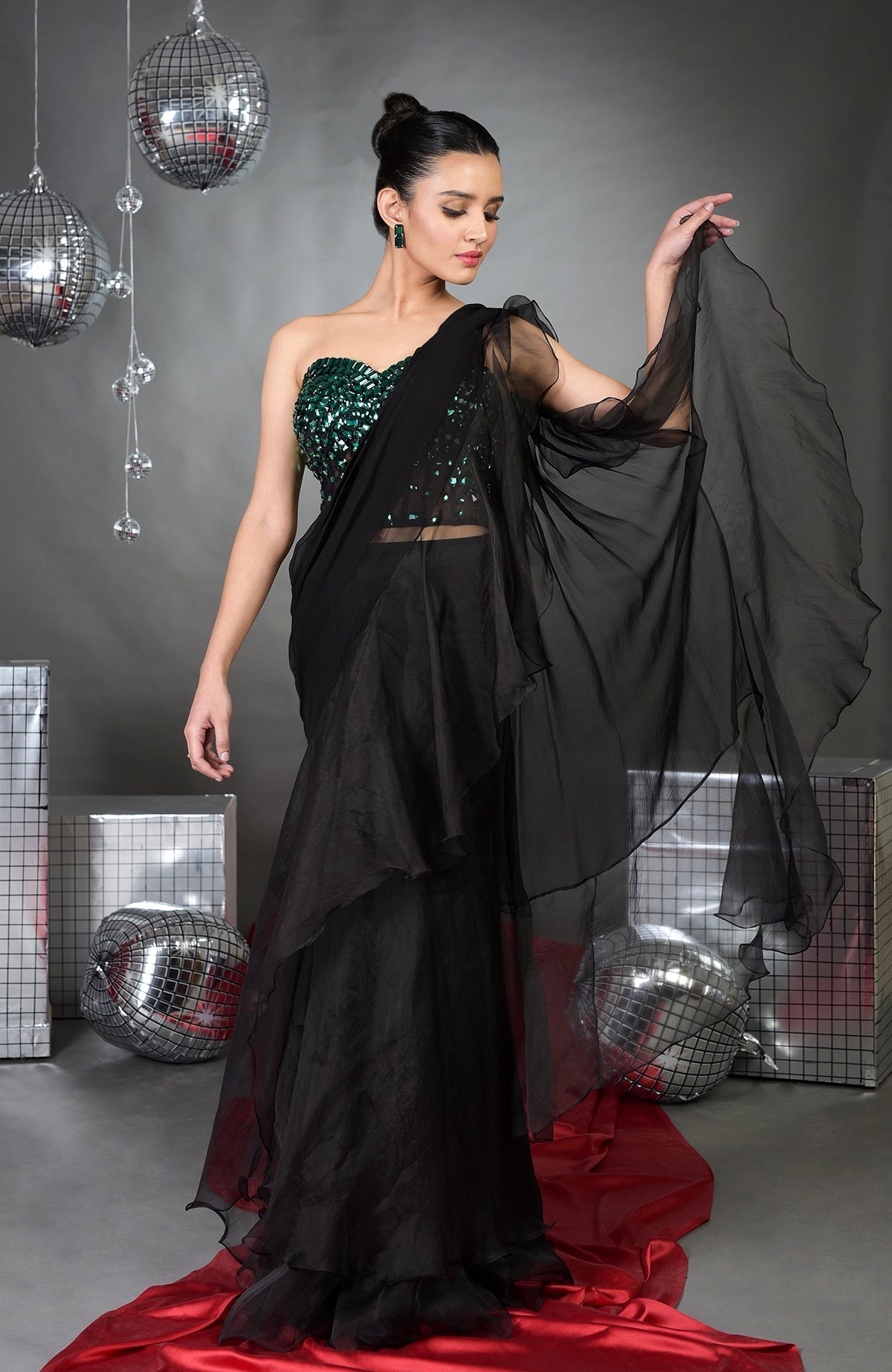 A woman models a black ruffled saree with an emerald green sequined corset.