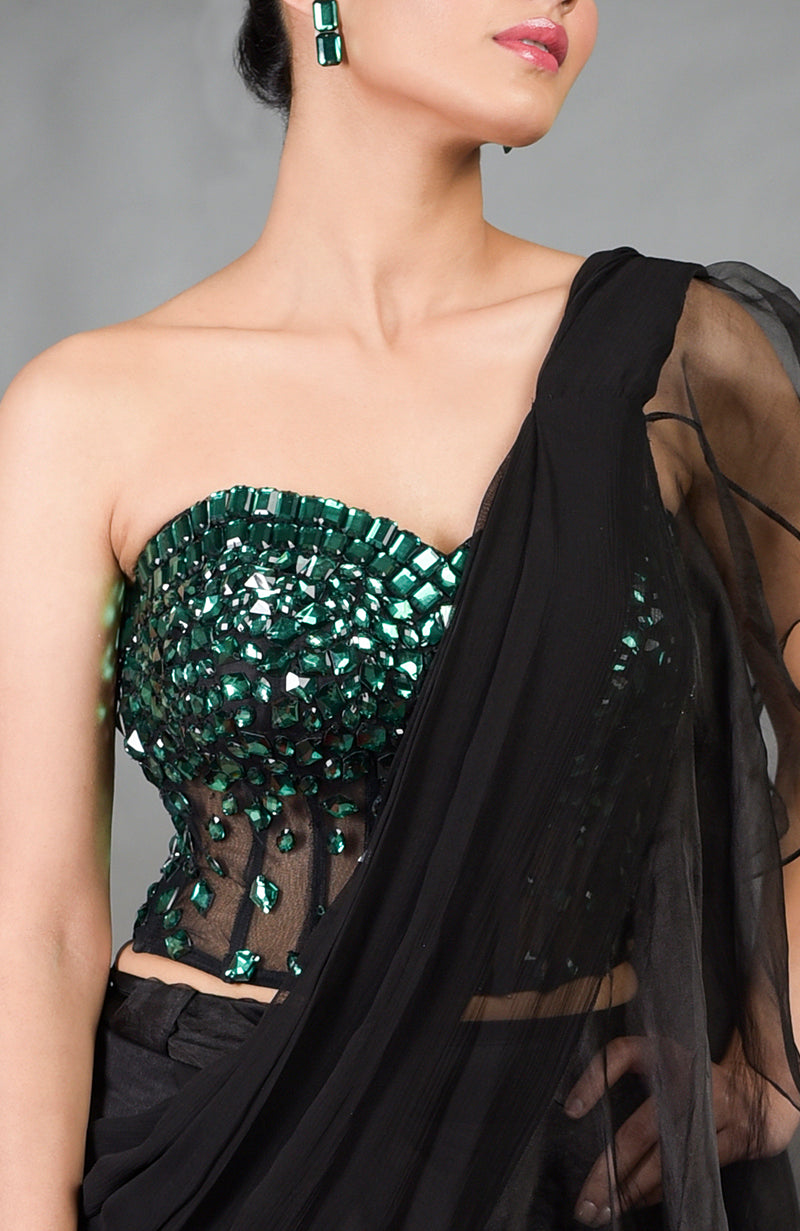 A woman models an emerald green hand-embroidered corset with a black ruffled saree.