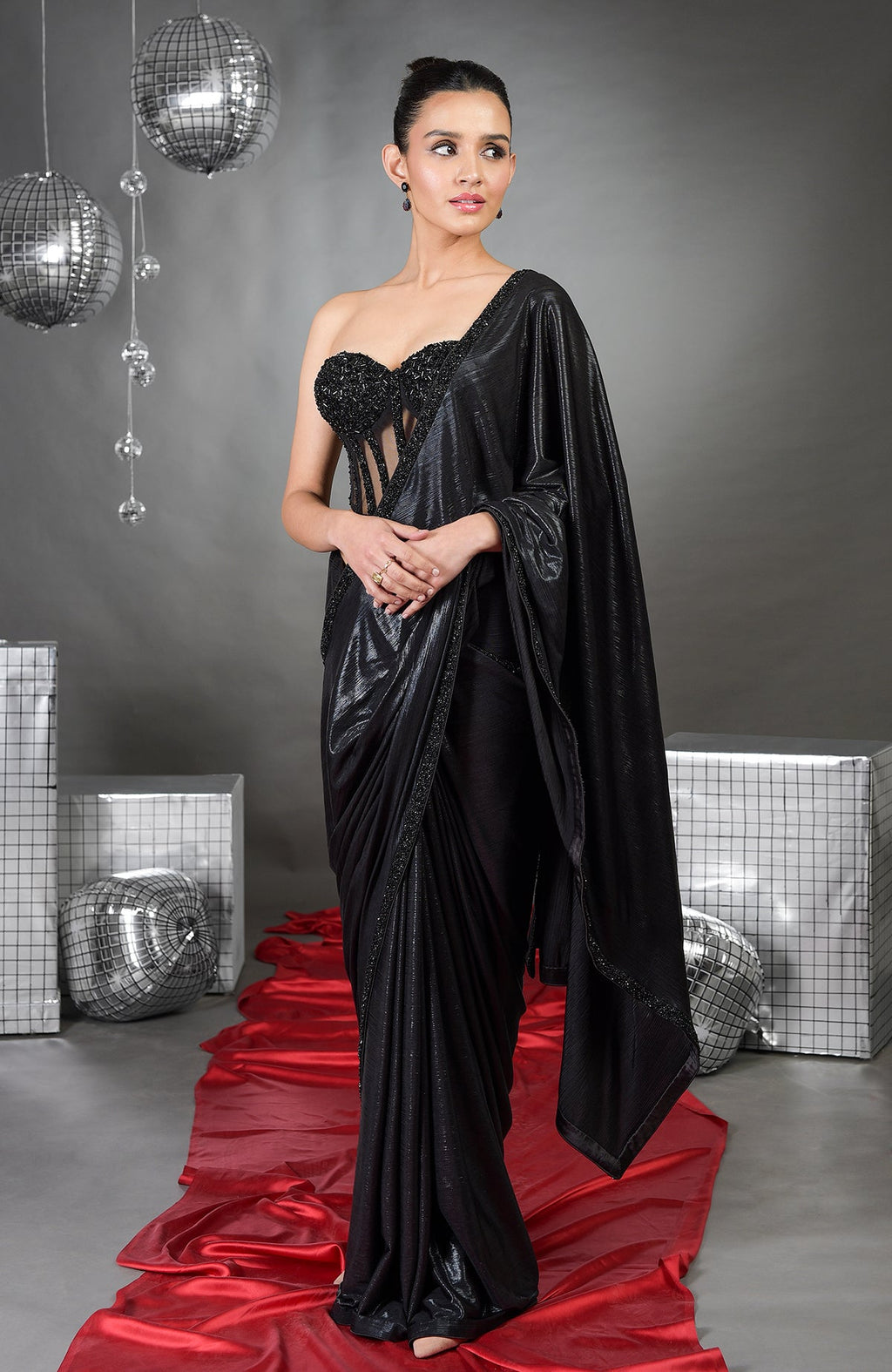 A woman in a black hand-embroidered corset saree set stands on a red fabric runner.