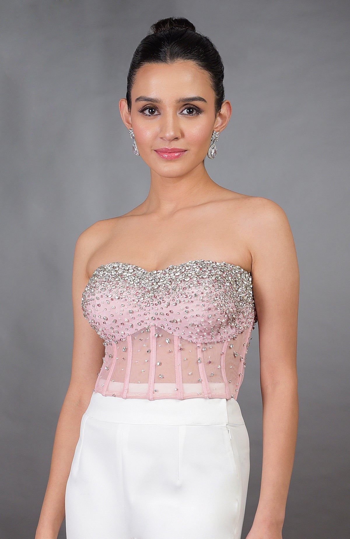 A woman models a pink hand-embroidered corset with white wide-leg pants.