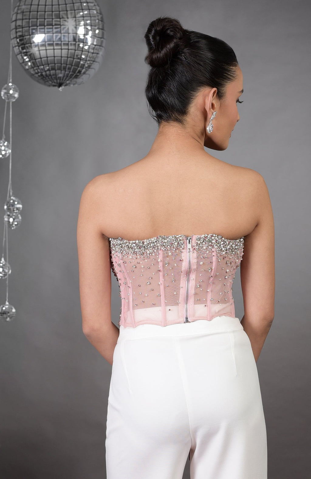 Back view of a woman in a pink hand-embroidered corset and white pants.
