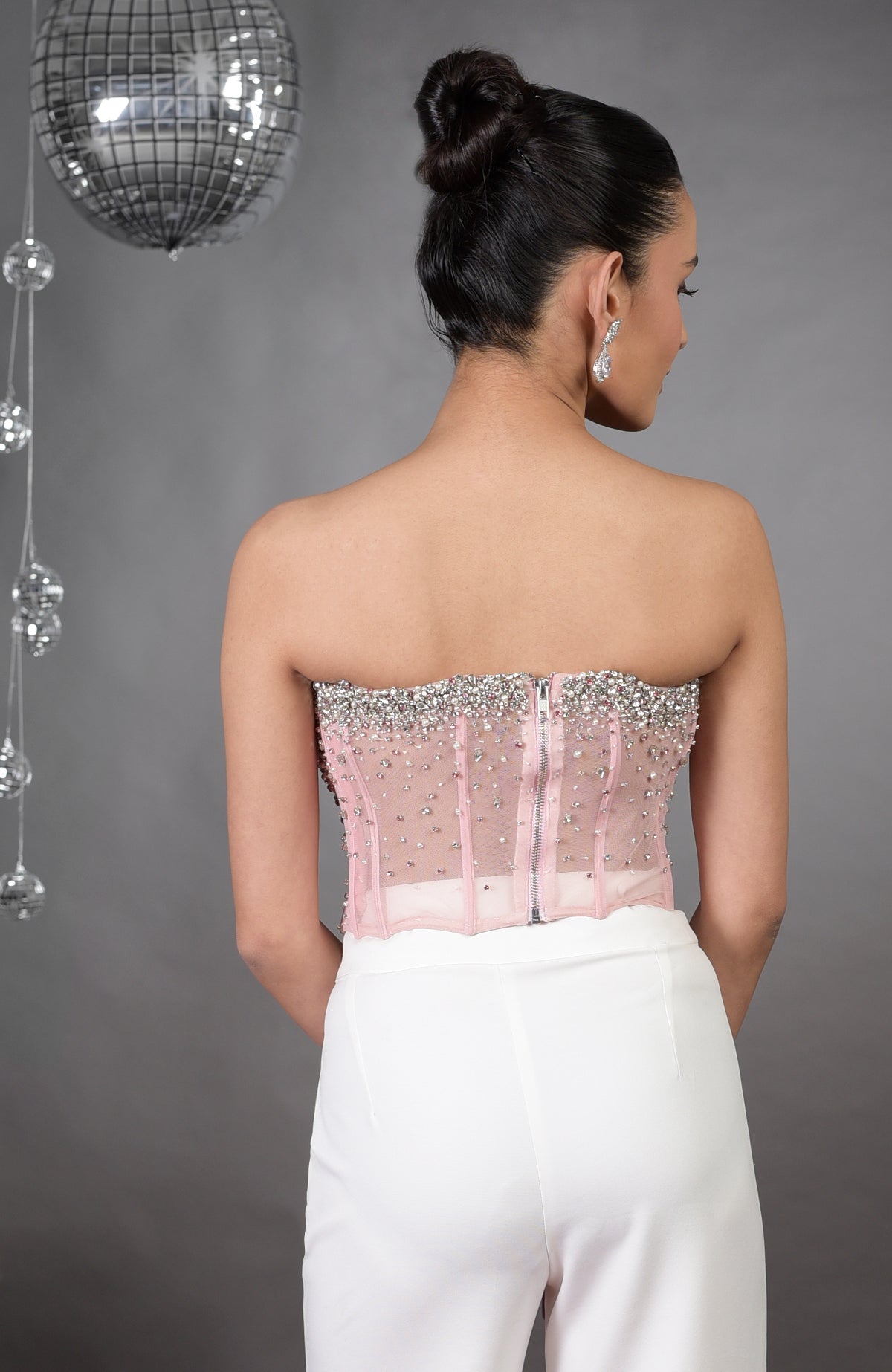 Back view of a woman in a pink hand-embroidered corset and white pants.