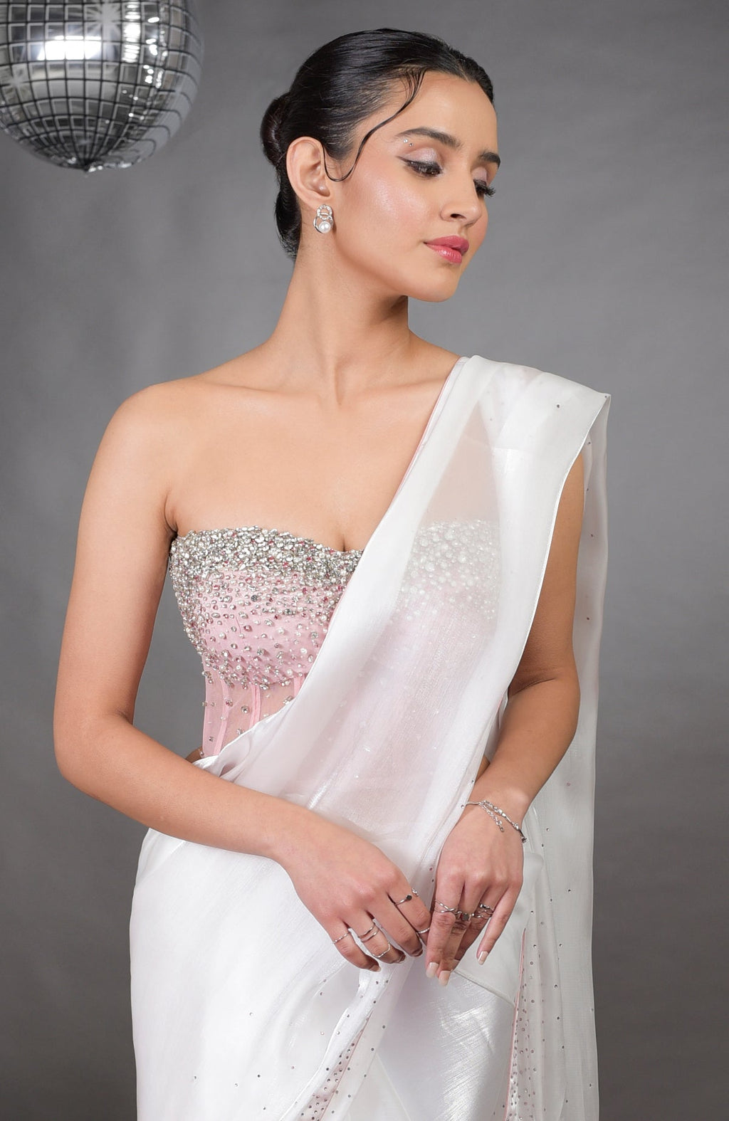A woman models a pink embroidered corset and a white silver light saree.