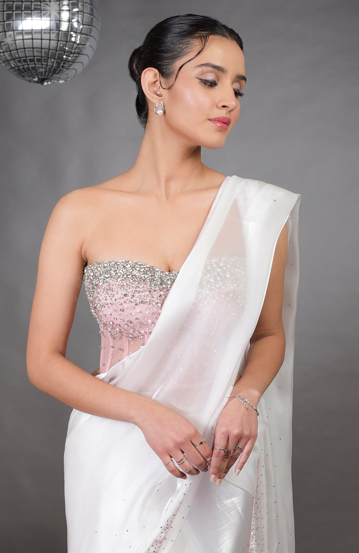 A woman models a pink embroidered corset and a white silver light saree.
