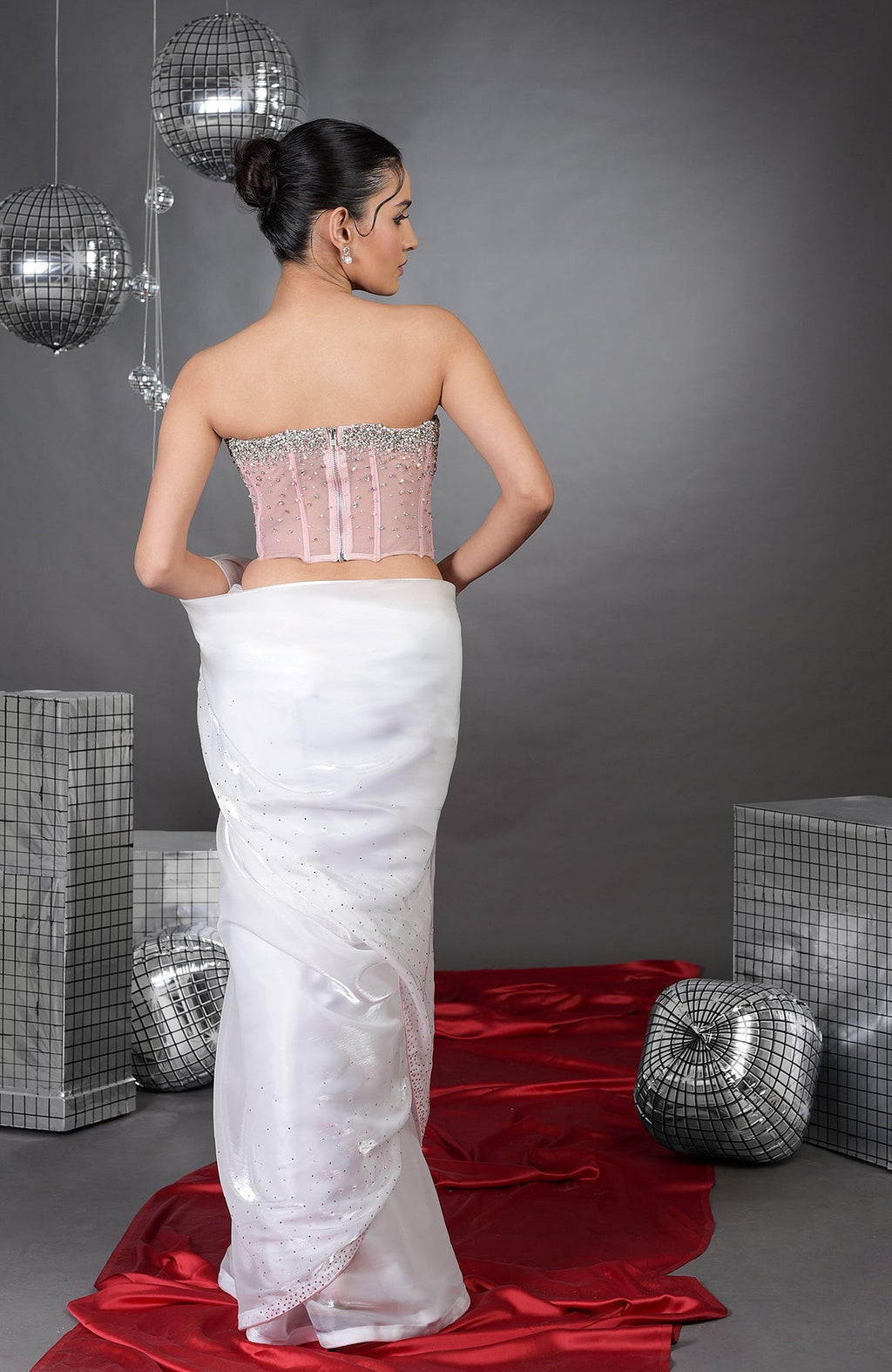 A woman models a pink embroidered corset and a white saree with silver accents.
