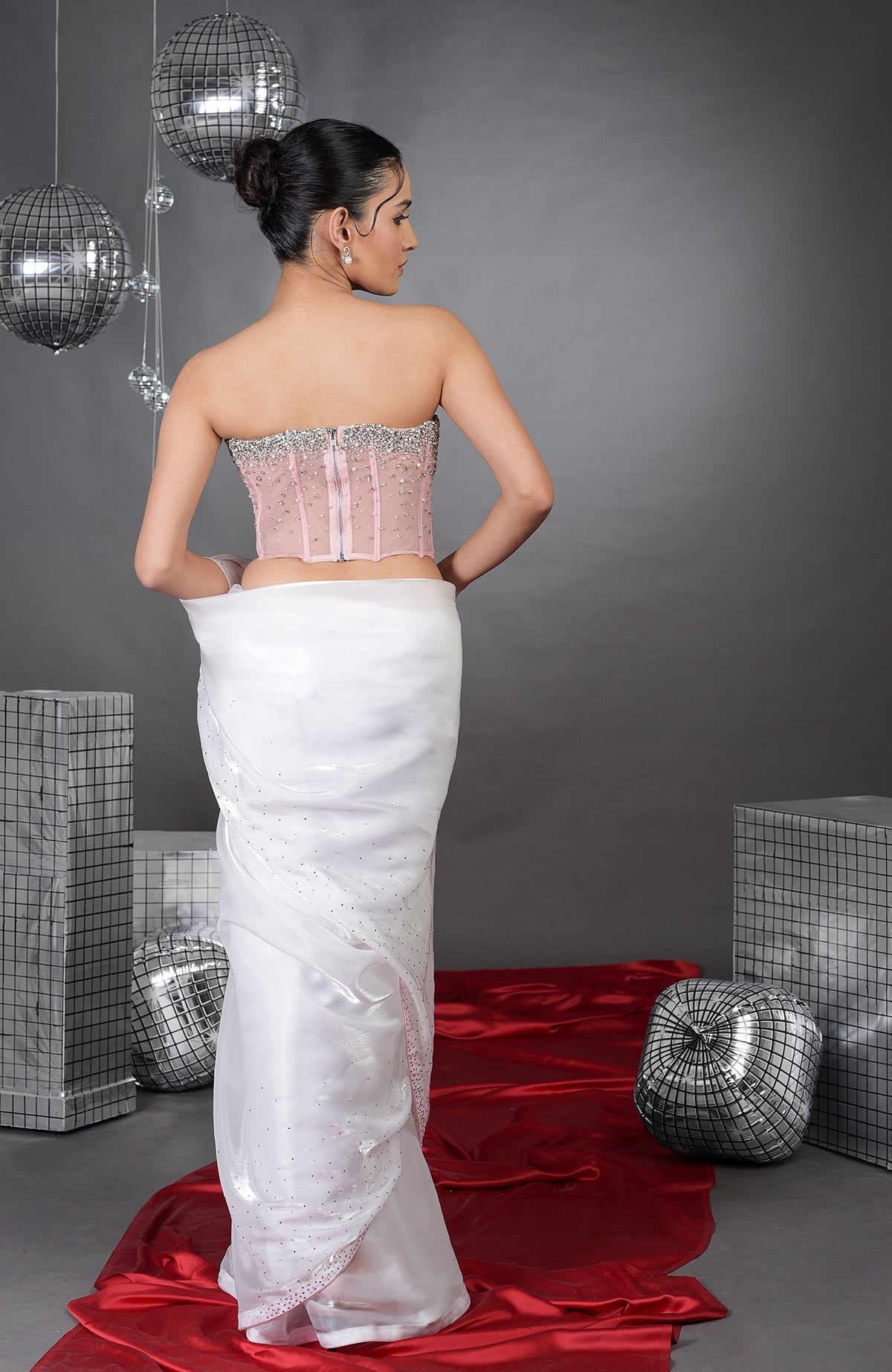 A woman models a pink embroidered corset and a white saree with silver accents.