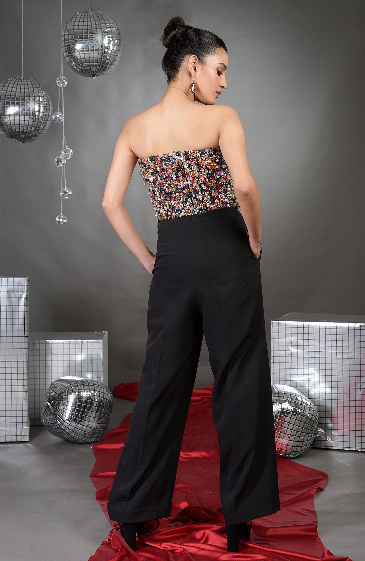 A woman models a strapless, multicolored crystal-embroidered corset with black high-waisted pants.