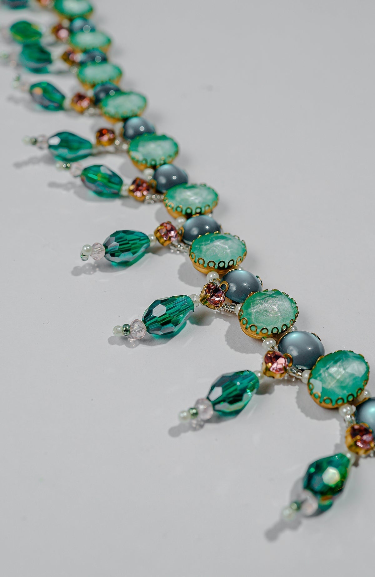 A close-up of a green jeweled crystal belt with pink accents on a white surface.