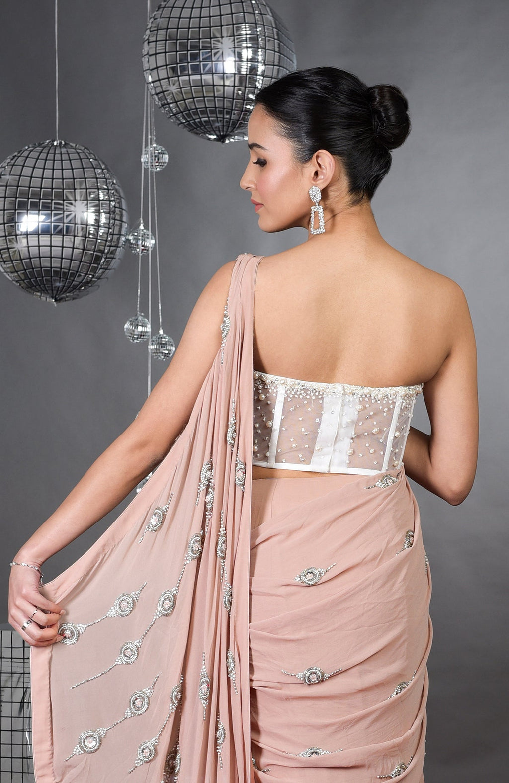 A woman from behind wears a nude pre-draped saree with a white embroidered corset.