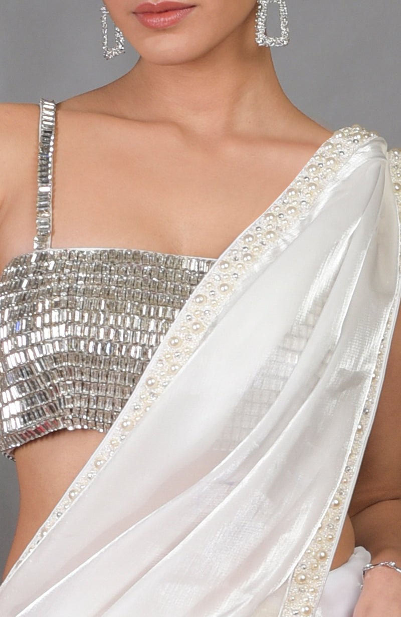A woman wears a silver crystal bustier and a white pearl-beaded saree.