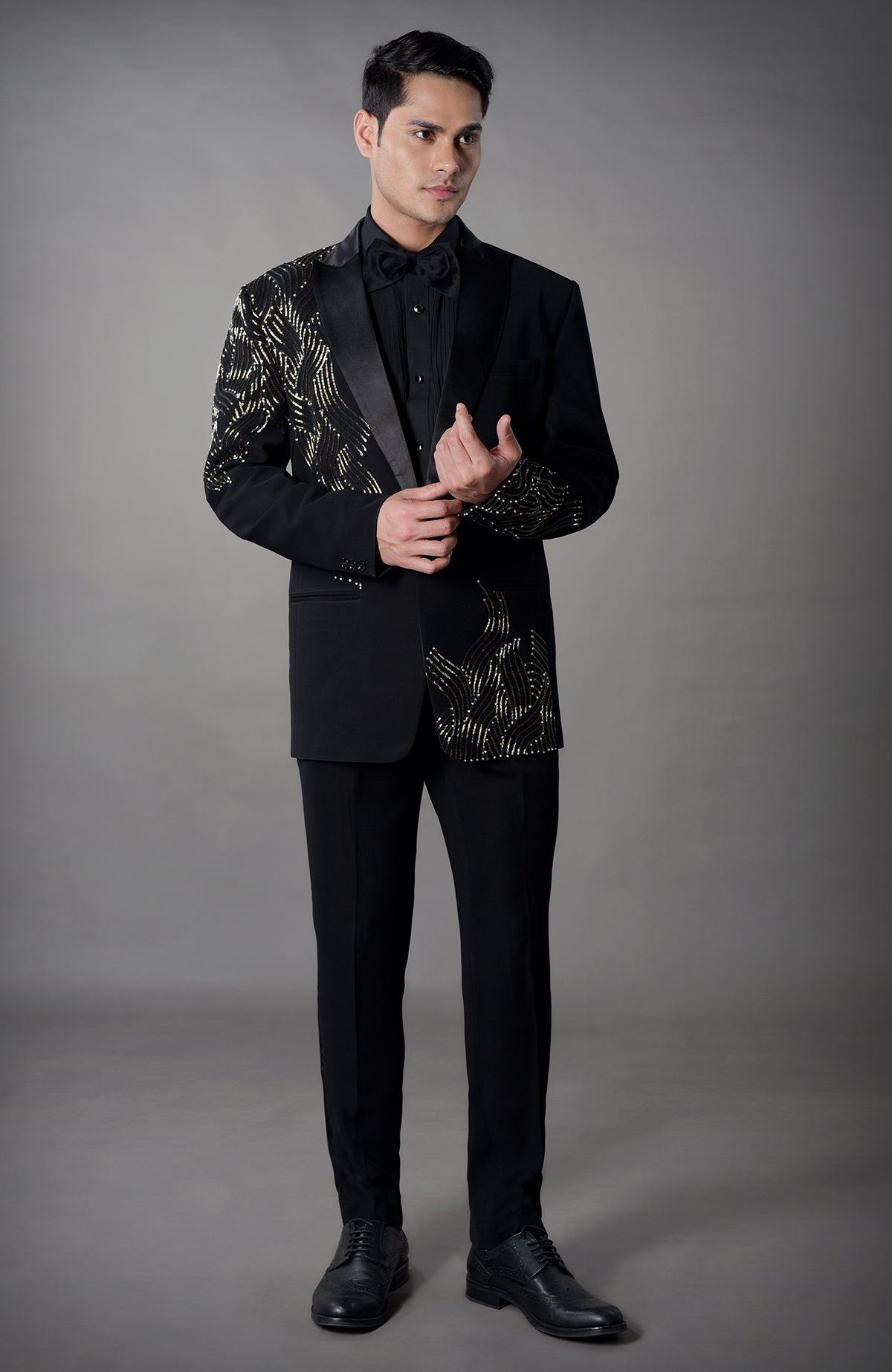 A man models a black tuxedo with gold partial shash embroidery.