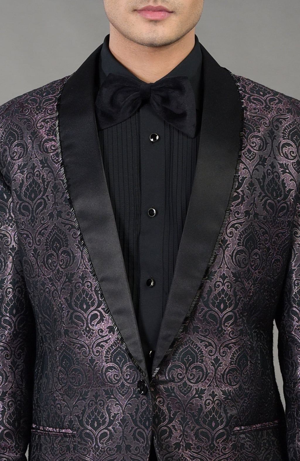 Man in a black brocade tuxedo with a black shirt and bow tie.
