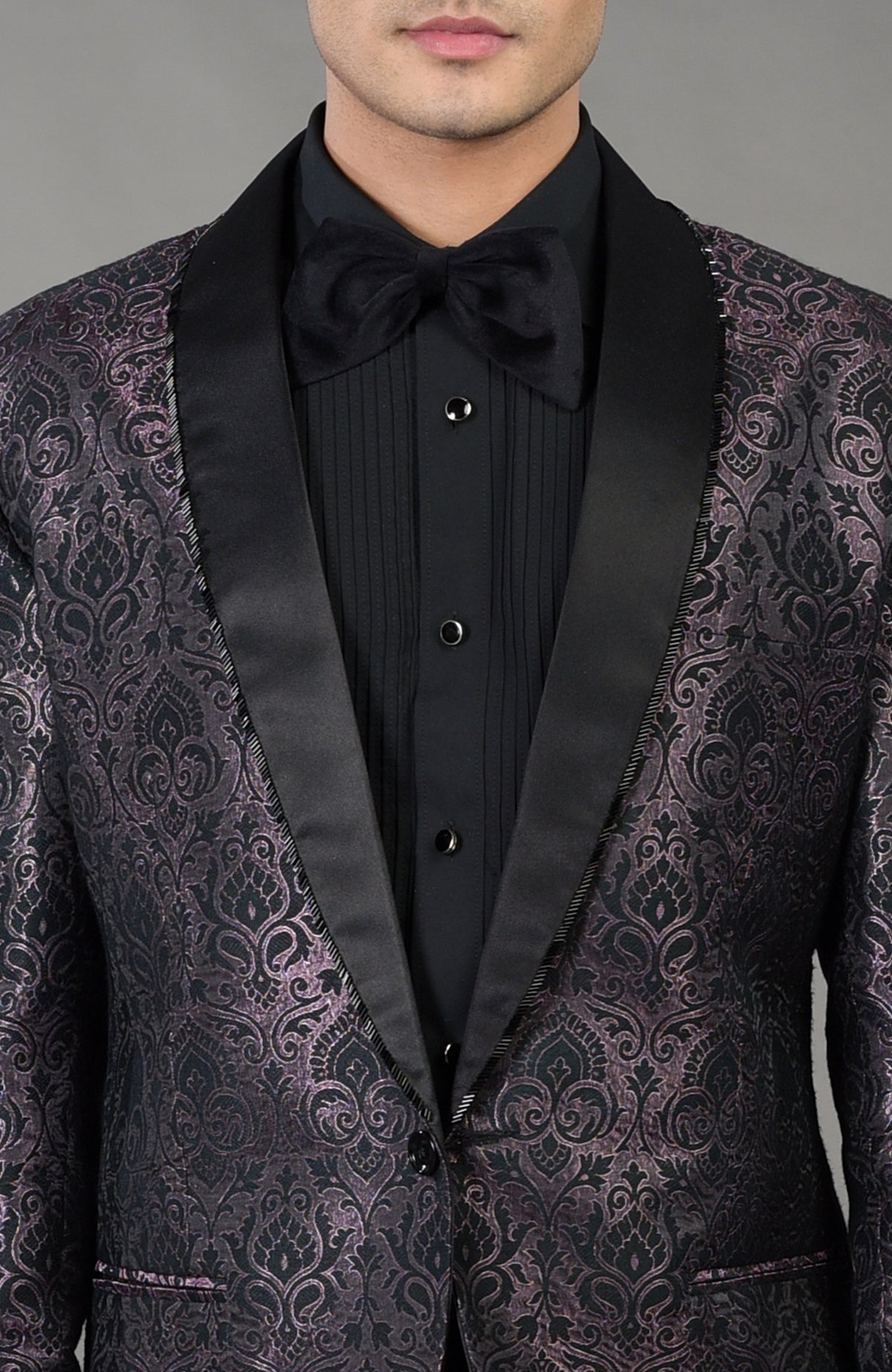 Man in a black brocade tuxedo with a black shirt and bow tie.