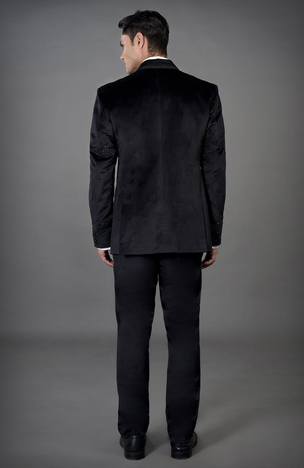 A man models a black velvet tuxedo set with intricate embroidery on the sleeves.