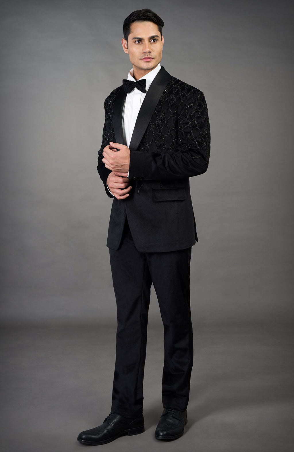 A man models a black tuxedo with an embroidered jacket and a white shirt.