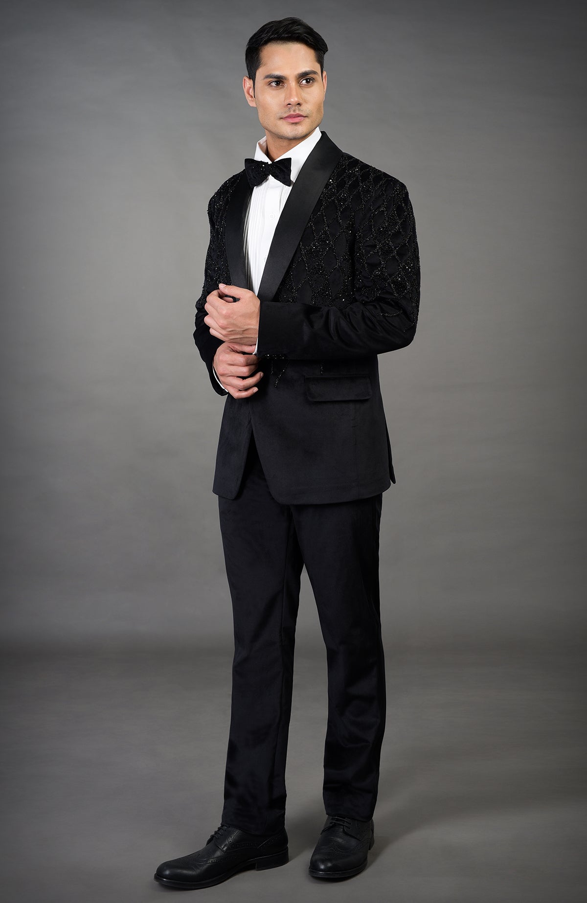 A man models a black tuxedo with an embroidered jacket and a white shirt.