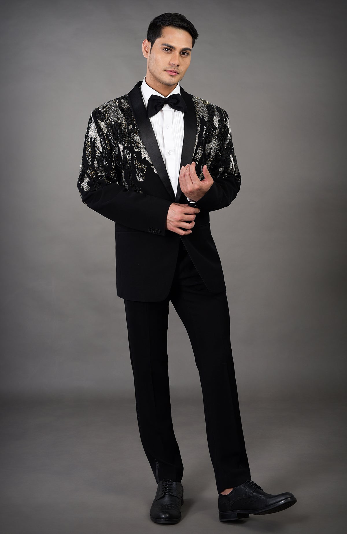 A man models a black tuxedo with a sequined abstract pattern on the jacket.