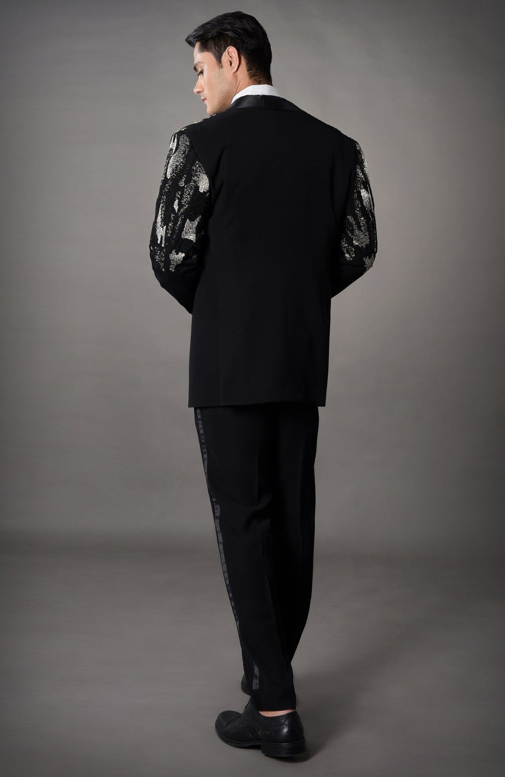 A man models a black tuxedo with silver sequin sleeves and black stripe pants.
