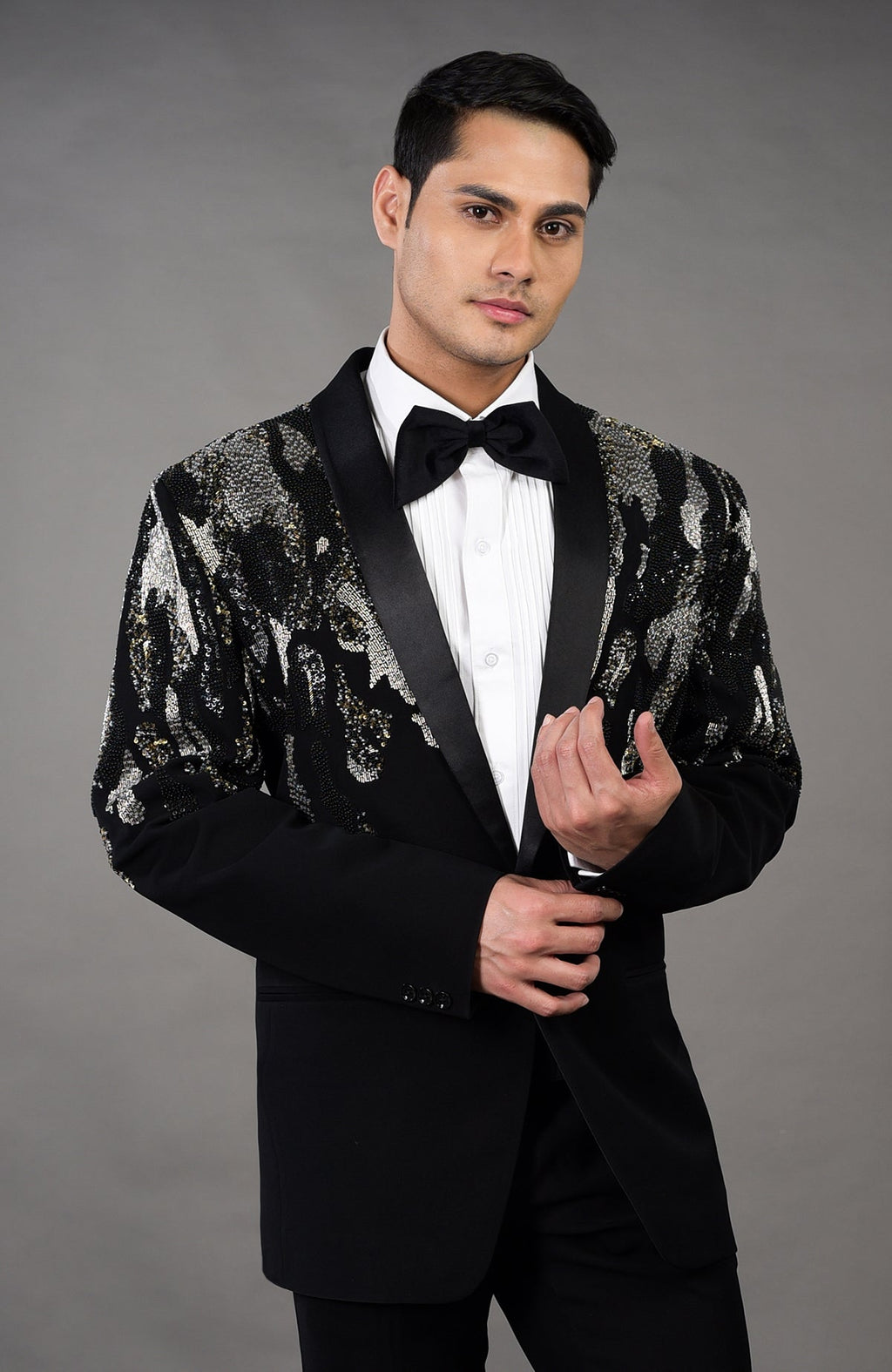 A man models a black tuxedo with a sequined abstract pattern on the shoulders and sleeves.