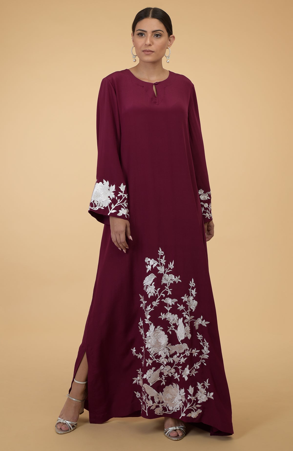 A woman models a burgundy kaftan with white floral and bird embroidery.