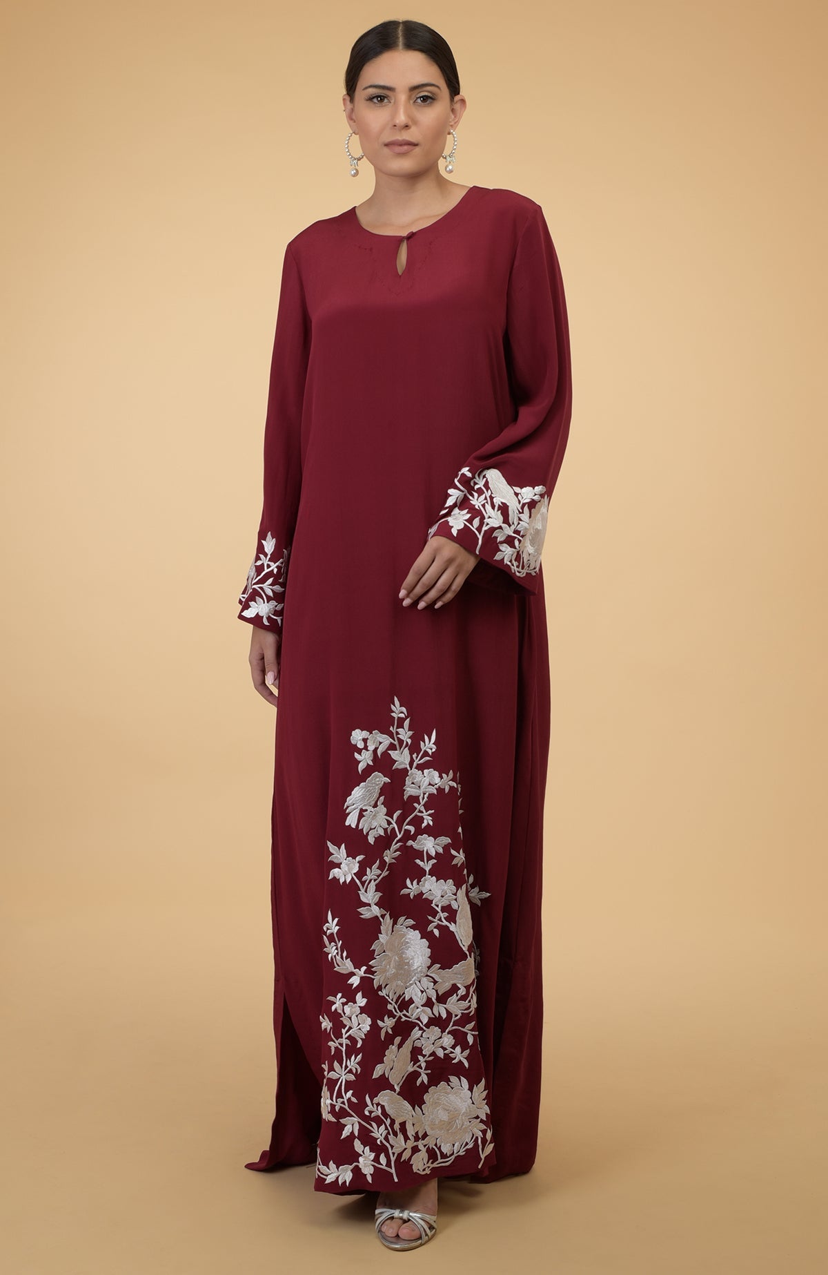 A woman models a maroon kaftan with silver floral and bird embroidery.