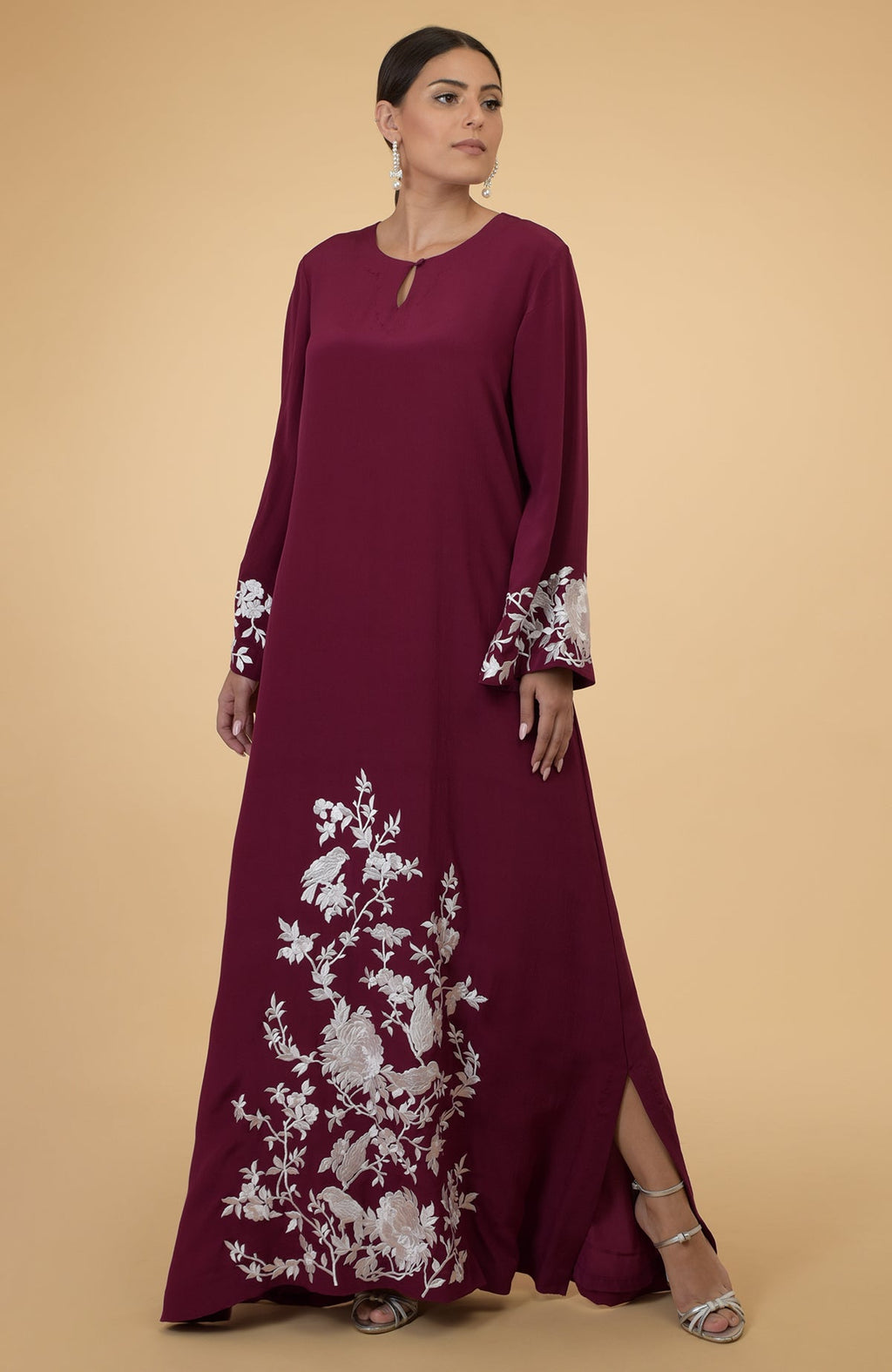 A woman models a burgundy kaftan with ivory floral and bird embroidery.