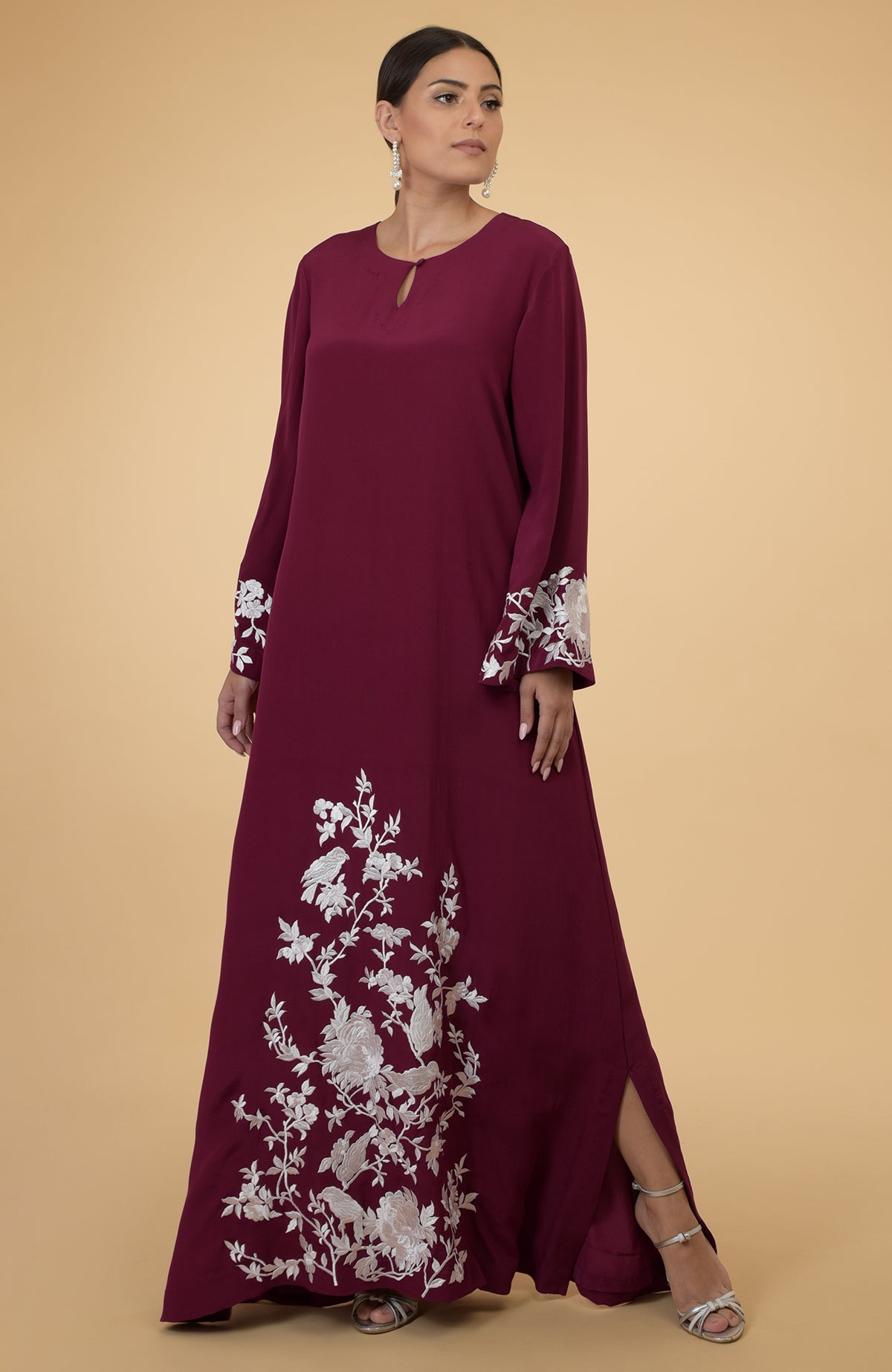 A woman models a burgundy kaftan with ivory floral and bird embroidery.
