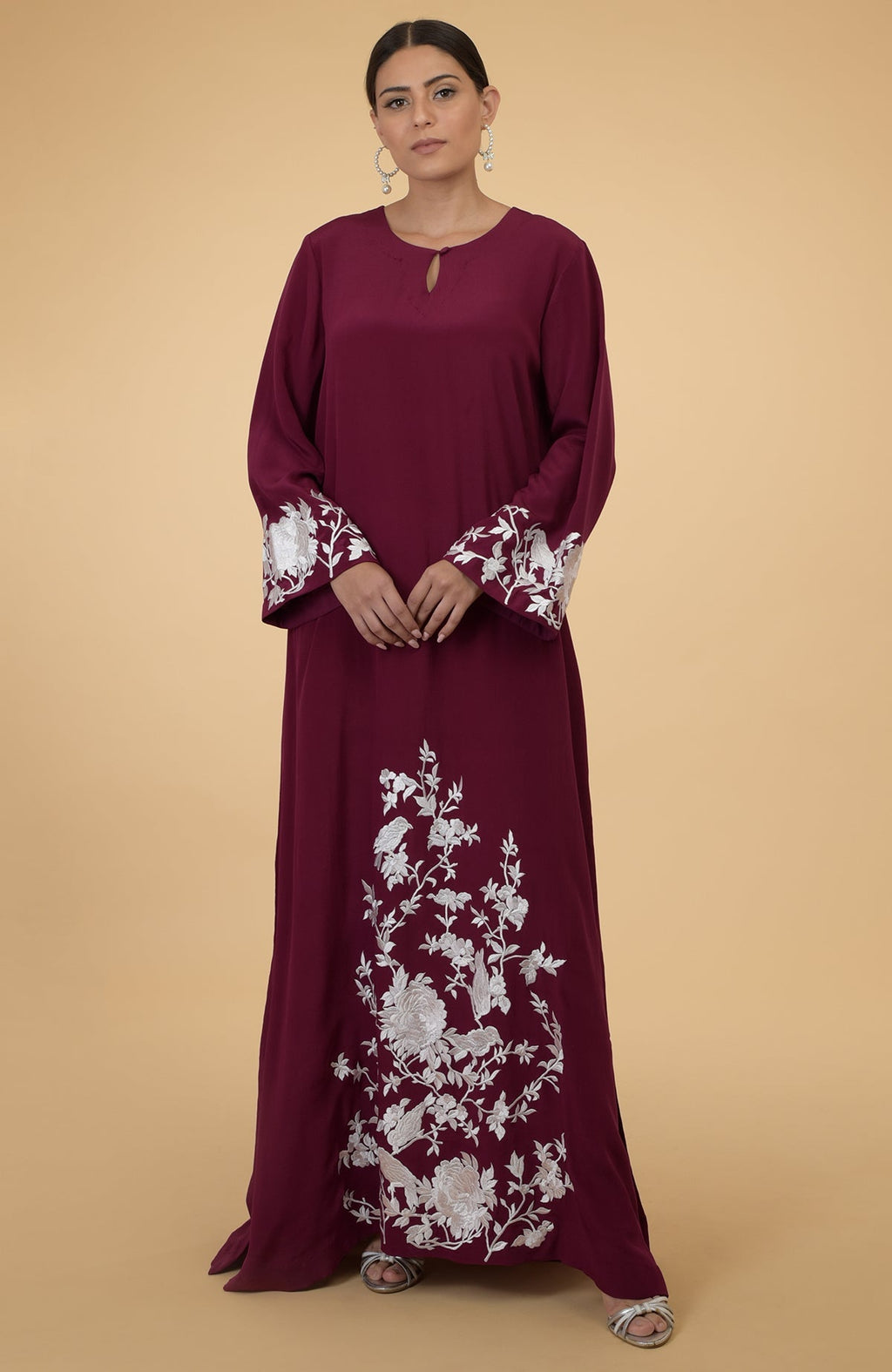Burgundy kaftan with ivory floral and bird embroidery, worn by a woman.