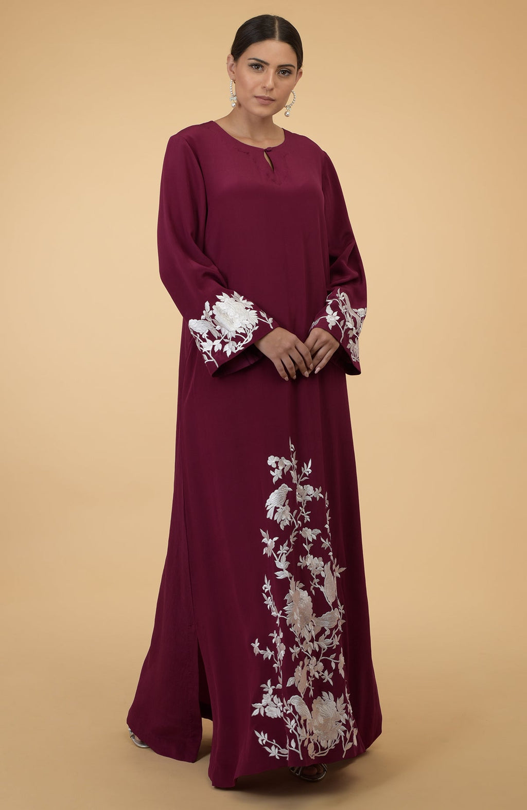 A woman models a burgundy kaftan with ivory floral and bird embroidery.