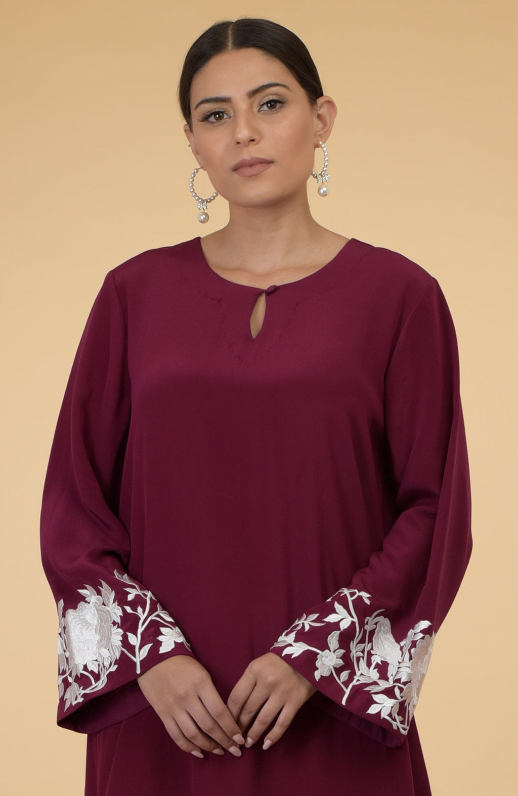 Burgundy kaftan with ivory floral and bird embroidery on the sleeves.