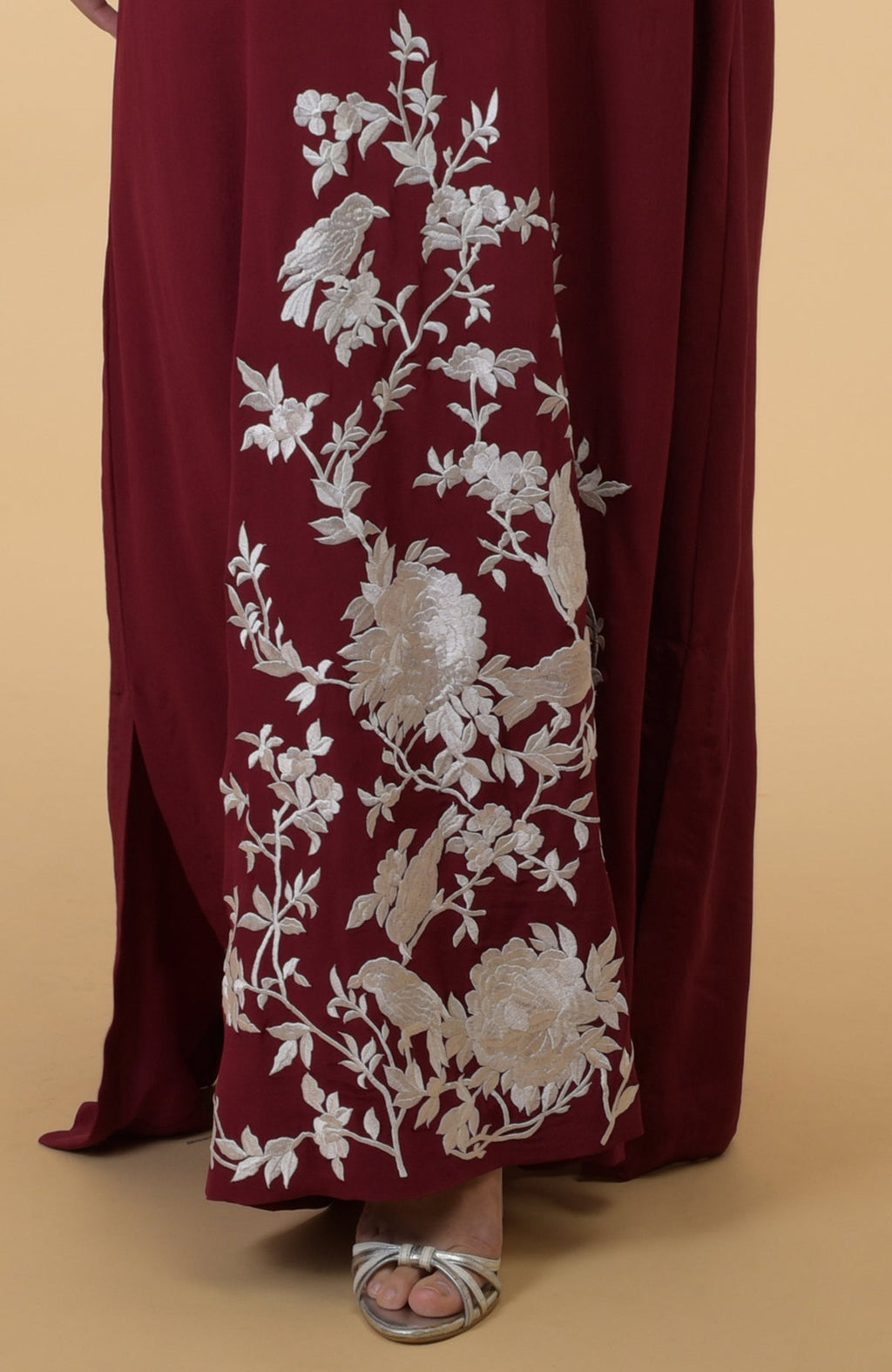 A burgundy kaftan with ivory floral and bird embroidery is shown on a model.