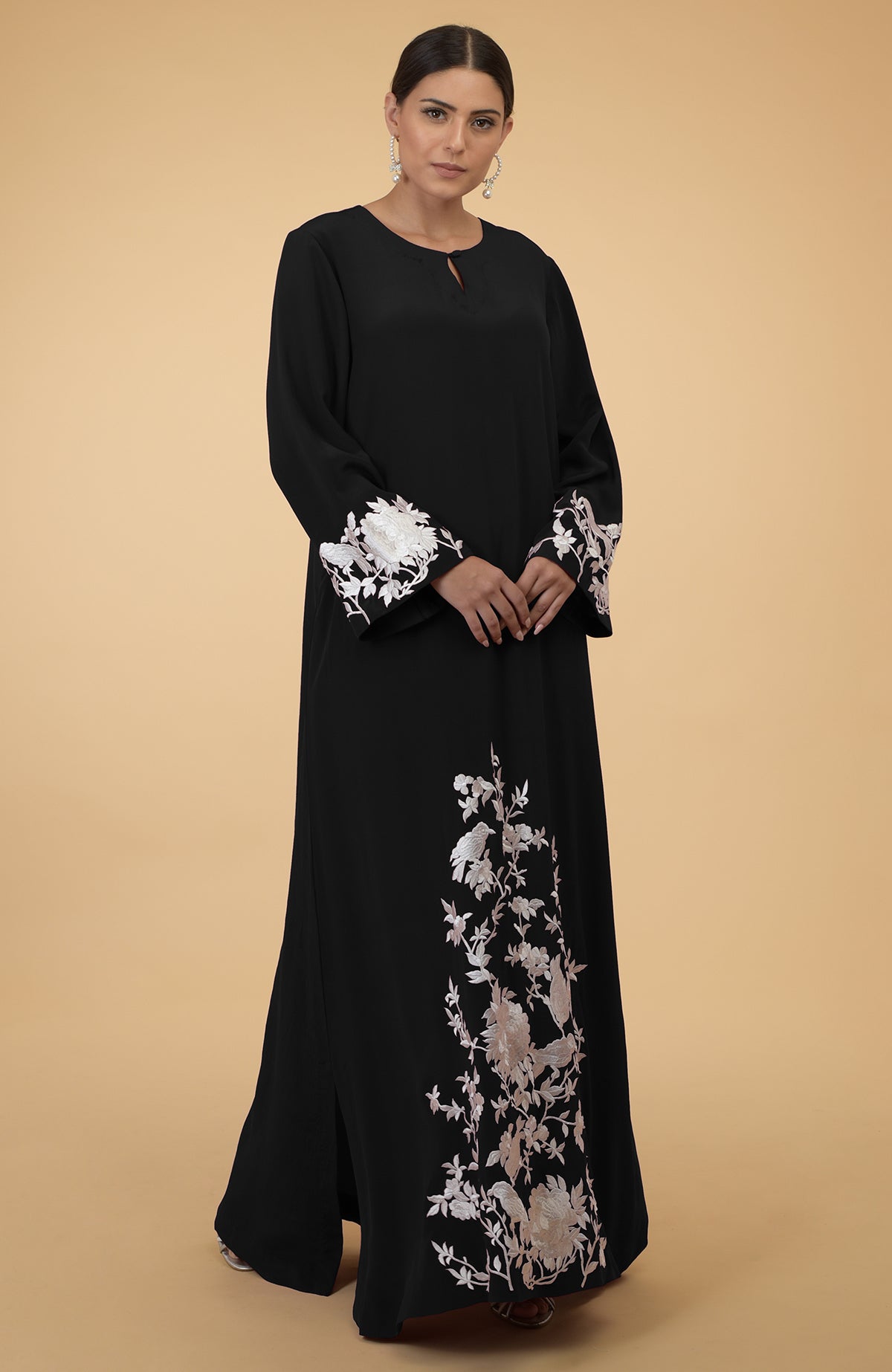 Black kaftan with ivory floral and bird embroidery, worn by a woman.