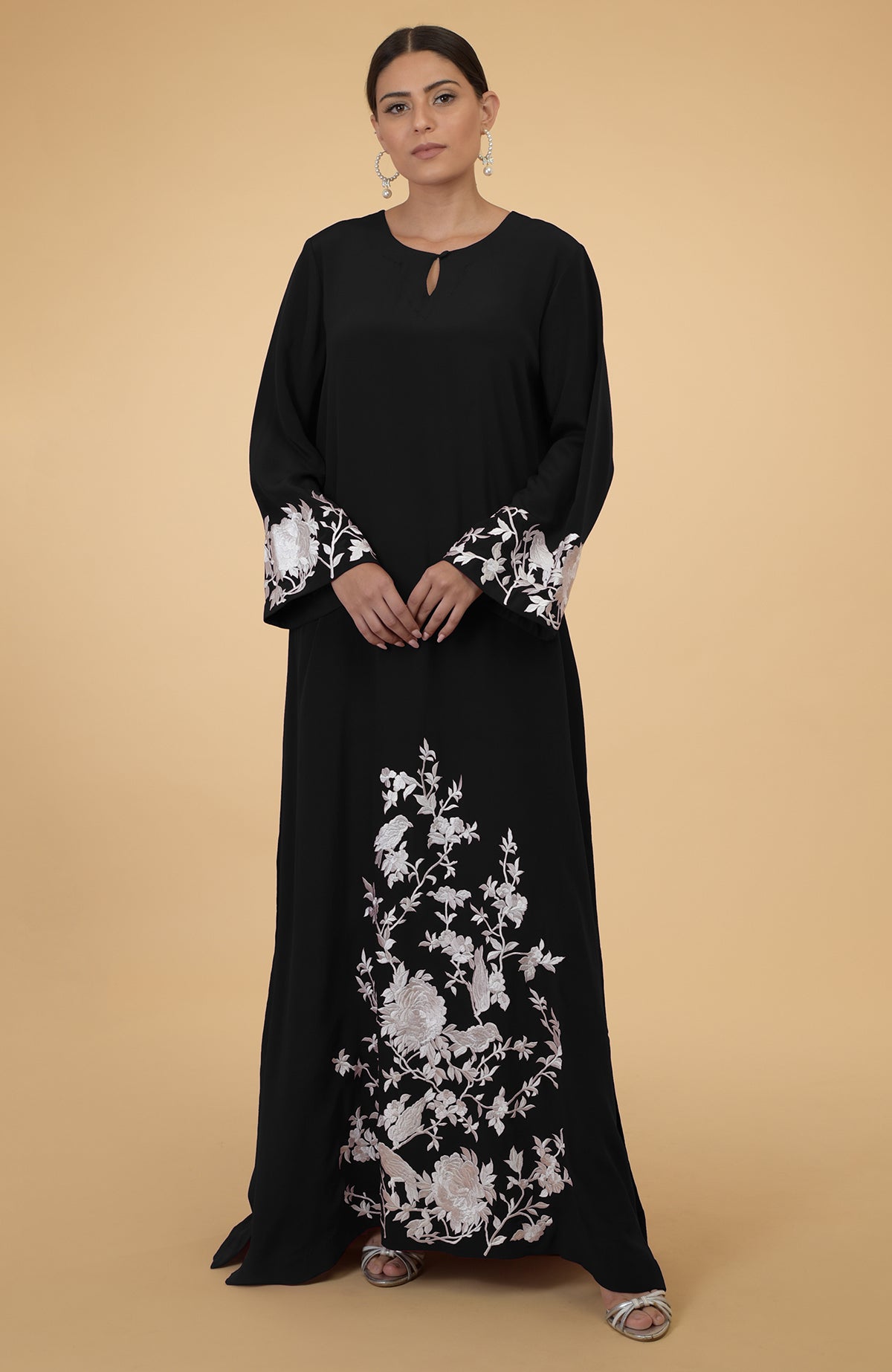 A woman models a black kaftan with white floral and bird embroidery.