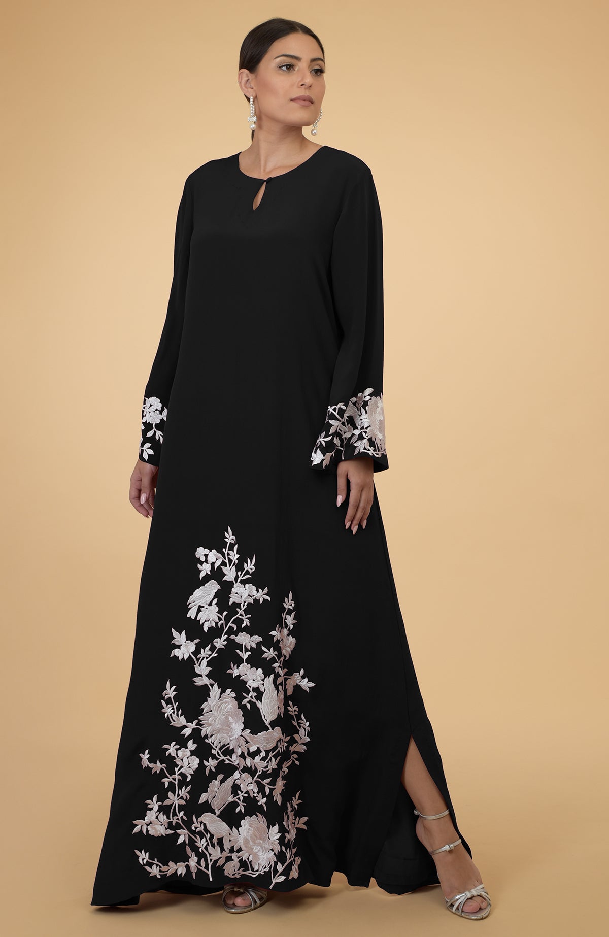 A woman models a black kaftan with ivory floral and bird embroidery.