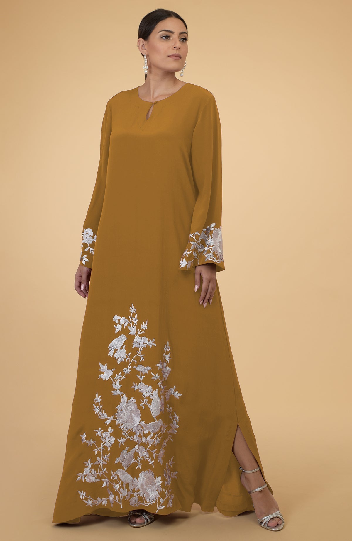 Muted mustard kaftan with floral and bird embroidery, worn by a woman.