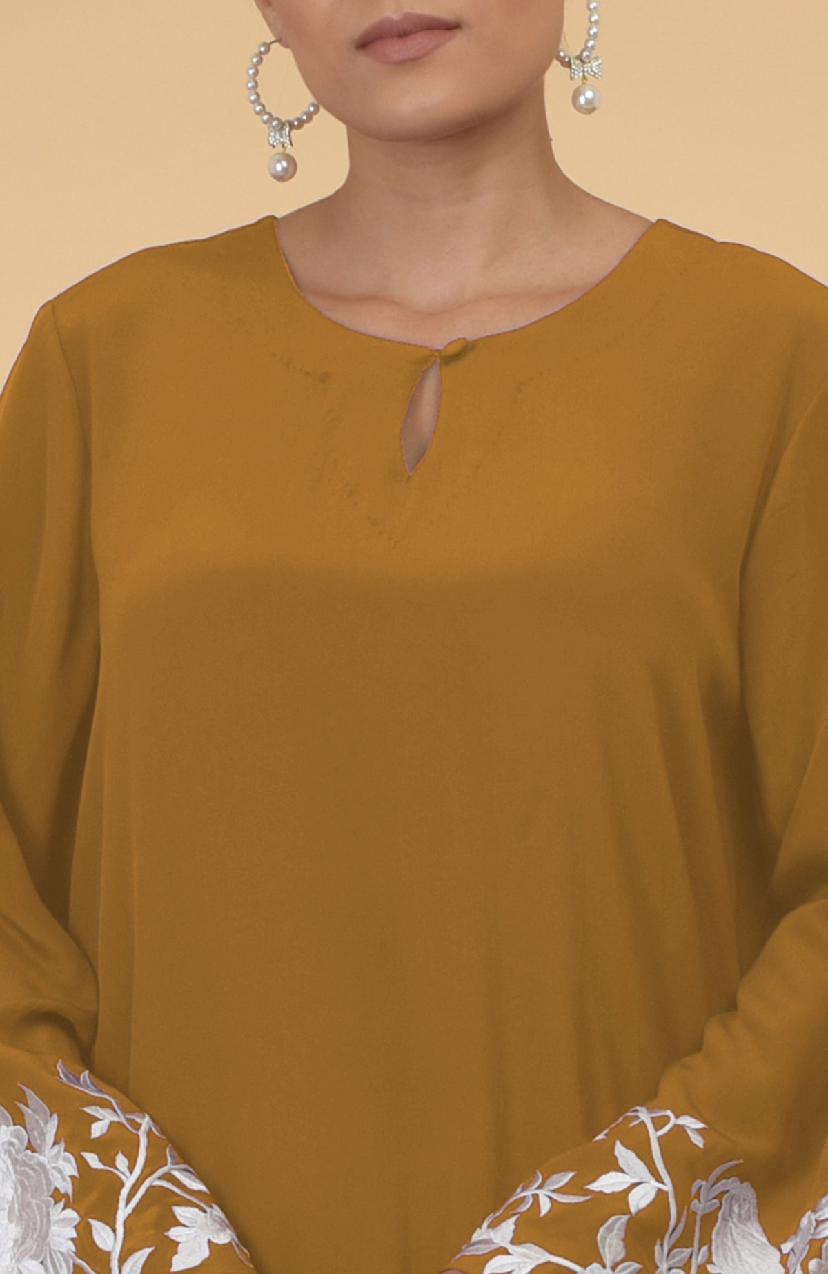 Muted mustard kaftan with a keyhole neckline and white floral and bird embroidery on sleeves.