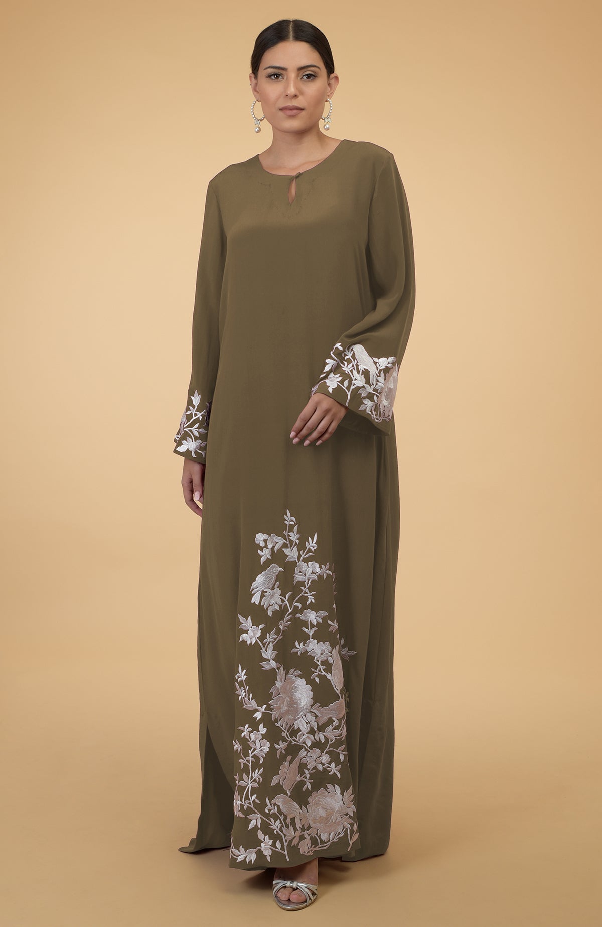 A woman models an Eclipse Blue floral and bird embroidered kaftan with silver sandals.