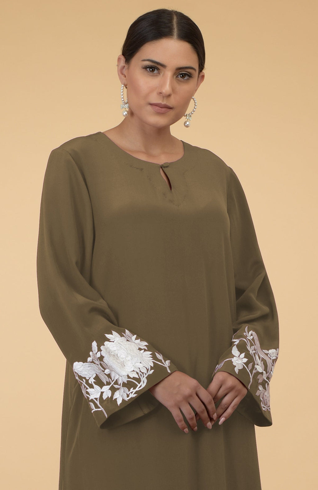 An olive silk crepe kaftan with white floral and bird embroidery on the sleeves.