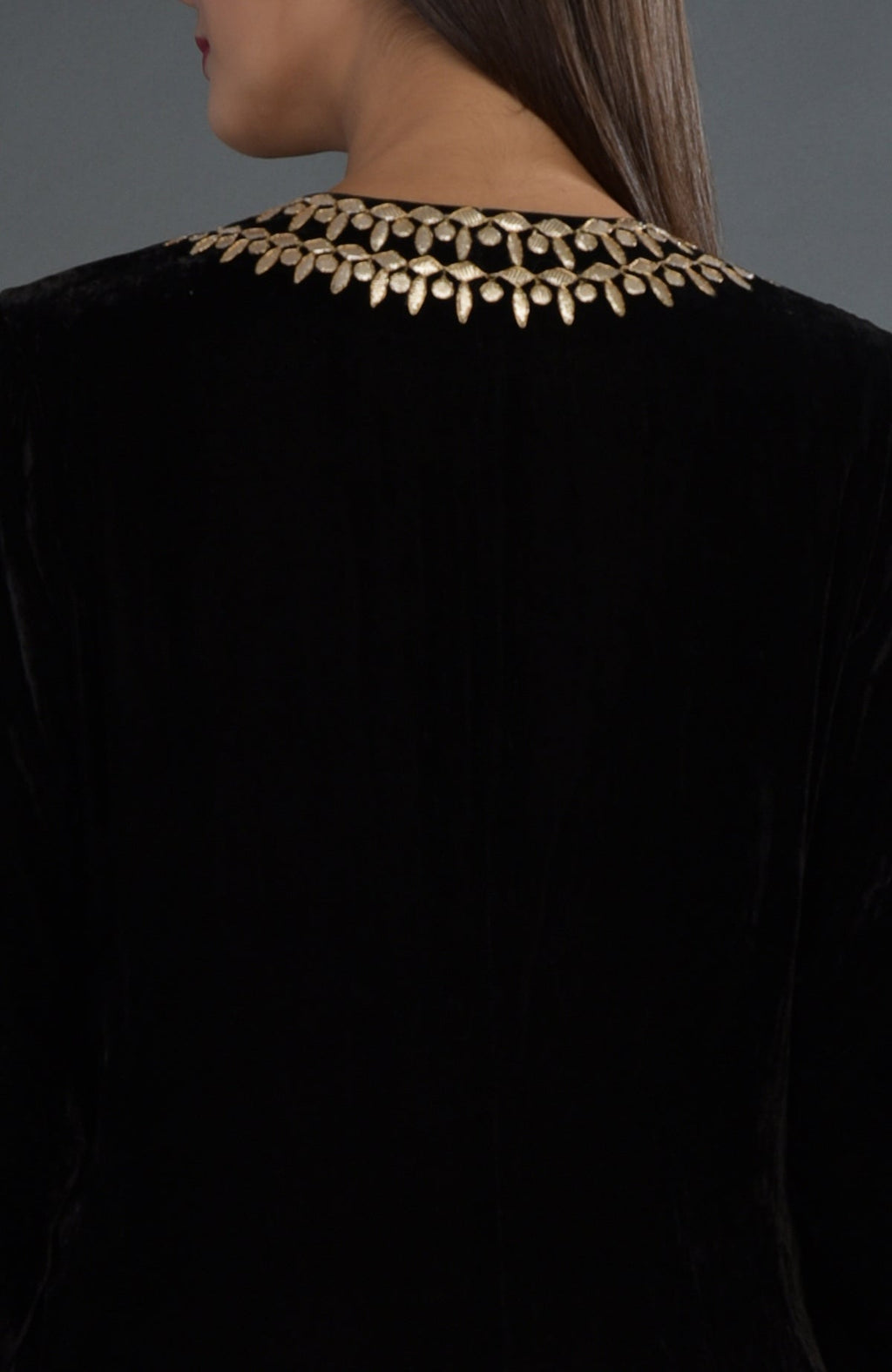 A woman models a black velvet jacket with gold embroidery on the neckline.