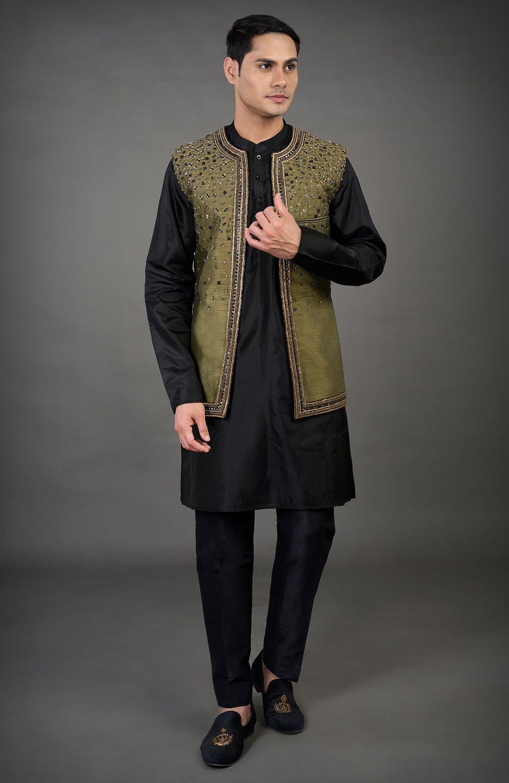A man models an olive hand-embroidered abstract jacket over a black kurta set.