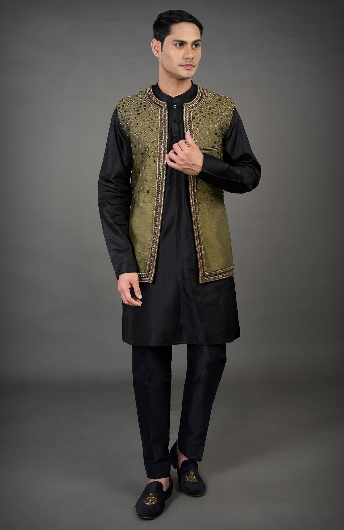 A man models an olive hand-embroidered abstract jacket over a black kurta set.