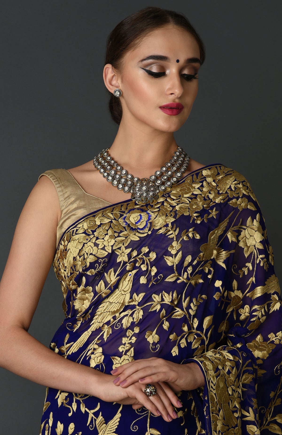 A woman models an indigo blue Parsi Gara hand embroidered saree with a gold blouse.