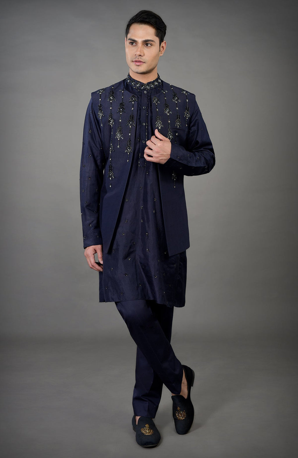 A man models a blue geometric hand-embroidered jacket set with matching shoes.