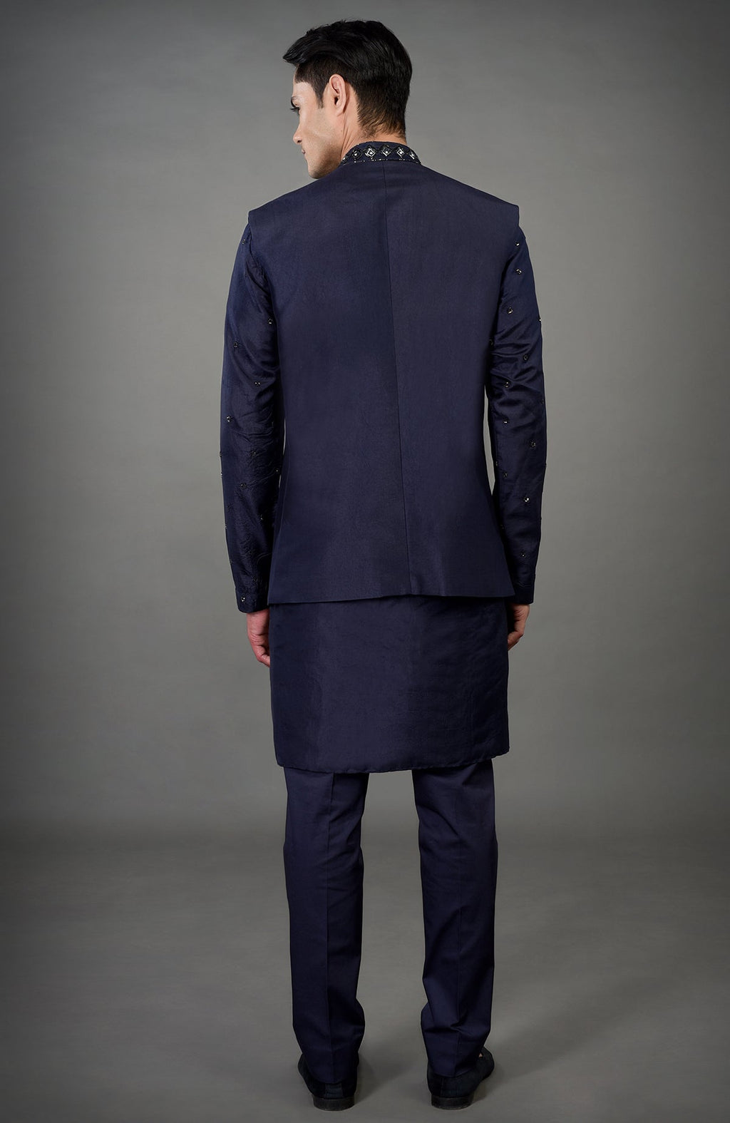 A man from behind wears a blue geometric hand-embroidered jacket set.