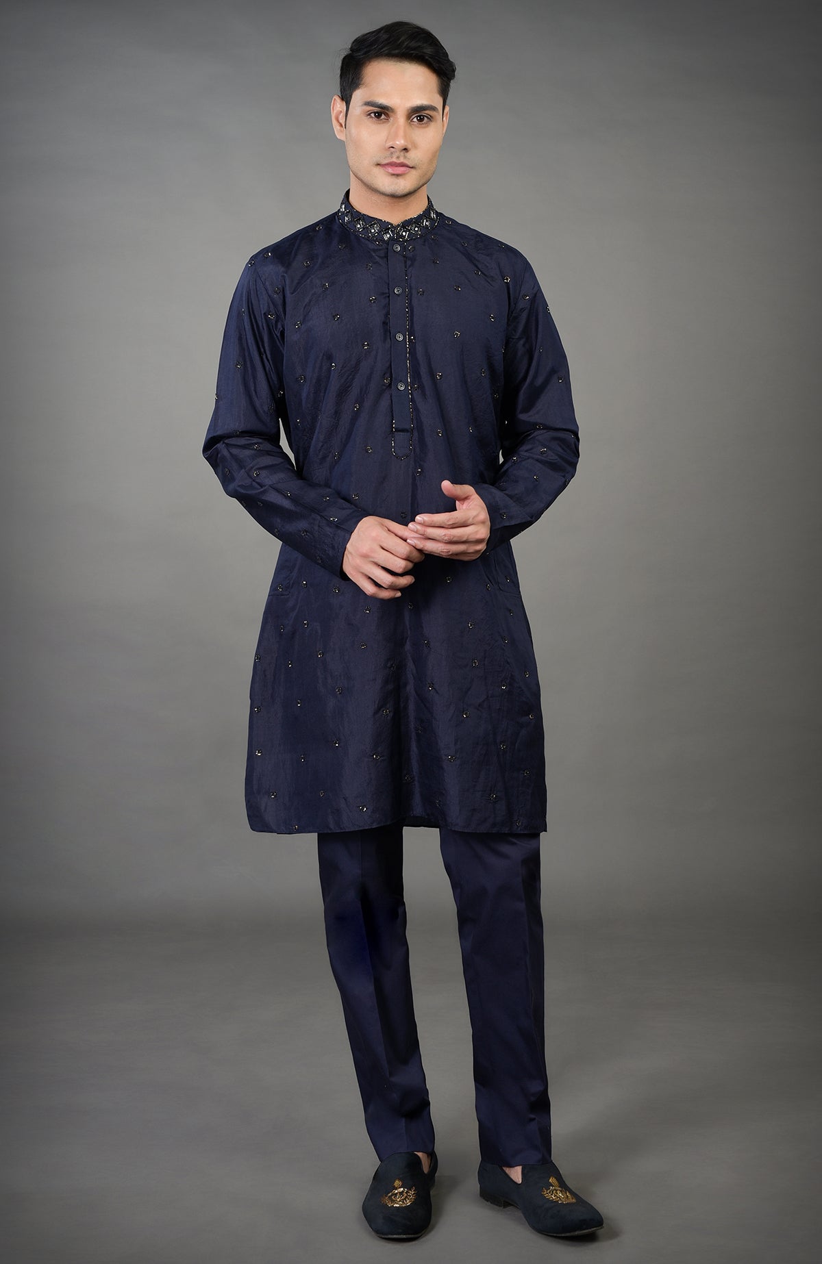A man in a blue geometric hand-embroidered kurta set with matching pants and shoes.